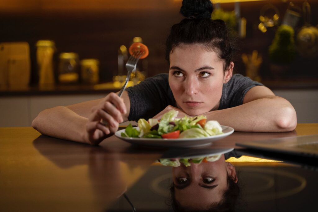 Donna seduta su un tavolo davanti a un piatto pieno di insalata.
